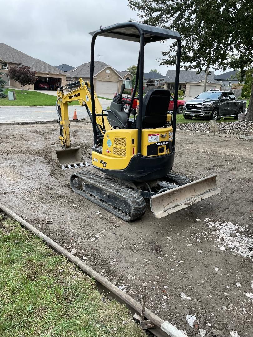 A small yellow excavator is sitting on top of a dirt field.