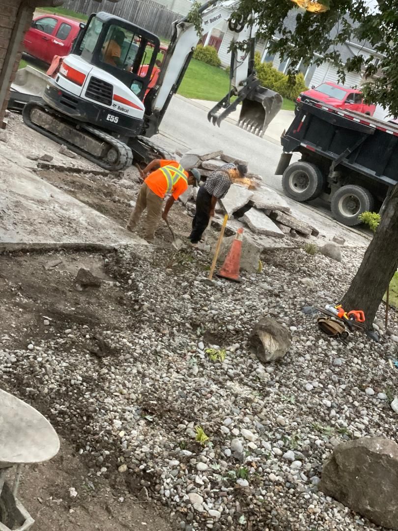 A group of construction workers are working on a sidewalk next to a dump truck.