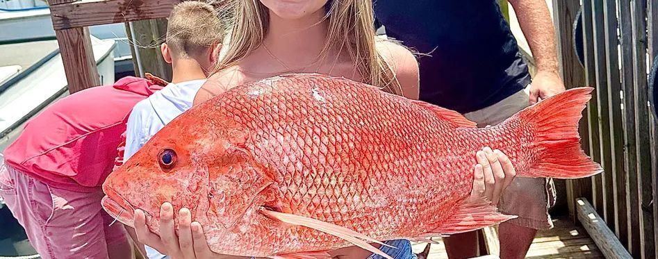 Teen holding a freshly caught red snapper on the Reel Groovy fishing boat during a deep sea fishing 