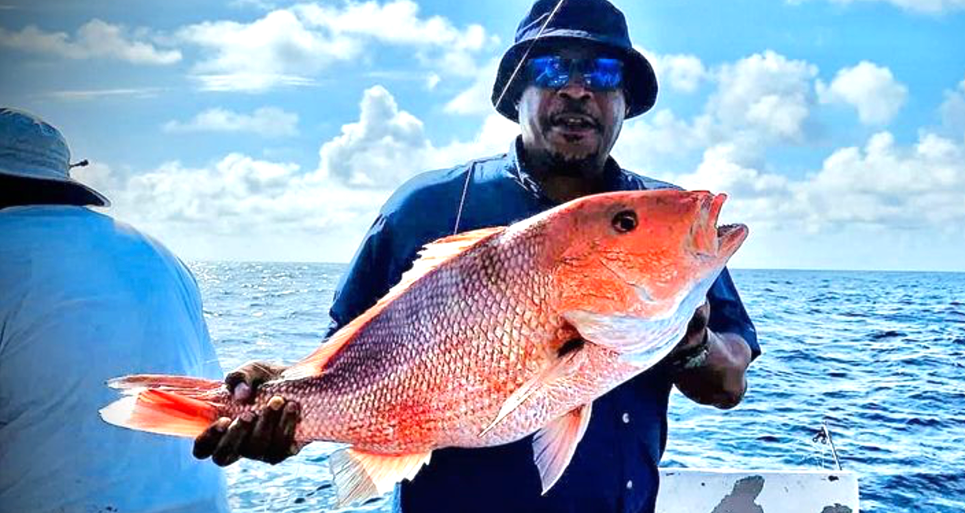 A man holding a large red snapper while on a deep sea fishing charter with Reel Groovy.