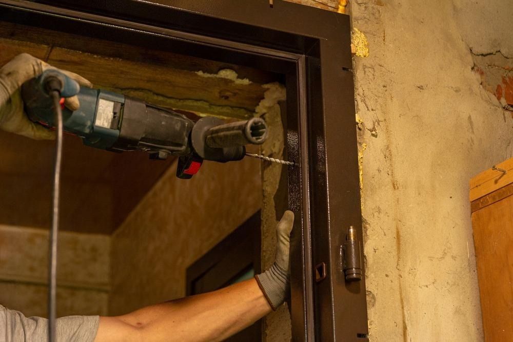 A man is using a drill to drill a hole in a door frame.