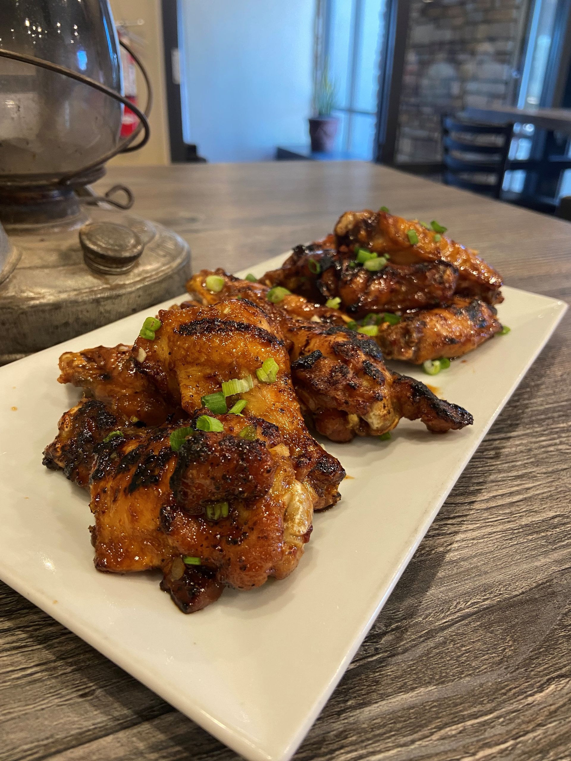 A white plate topped with chicken wings and green onions on a wooden table.
