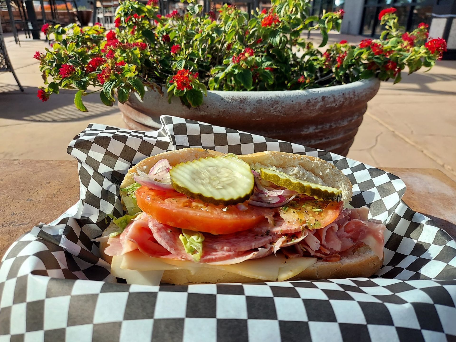A sub sandwich with pickles and tomatoes on a checkered paper on a table.