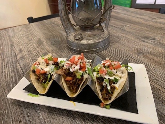 Three tacos are sitting on a white plate on a wooden table.