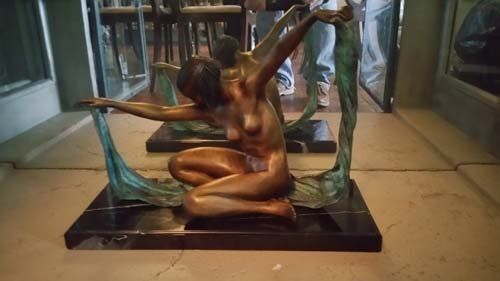 Bronze sculpture of a nude figure kneeling, arms outstretched between stylized elements, on a black base.