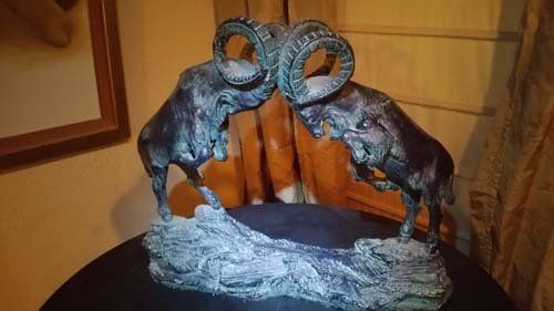 Bronze sculpture of two rams headbutting on a rocky base.