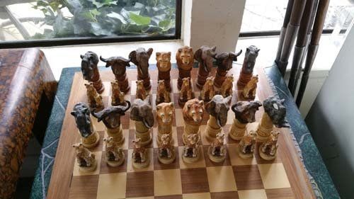Chess set with animal-shaped pieces on a checkered board, near a window and wooden objects.