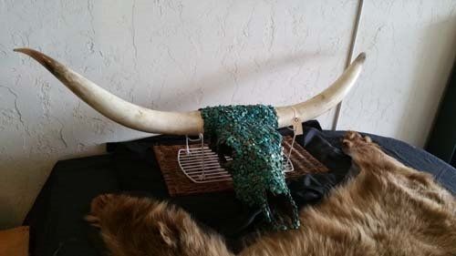 A longhorn skull with turquoise glitter, resting on a brown fur pelt and wicker.