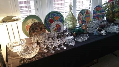 Display of crystal glassware, plates, and a decorative bottle on a black tablecloth in front of windows.