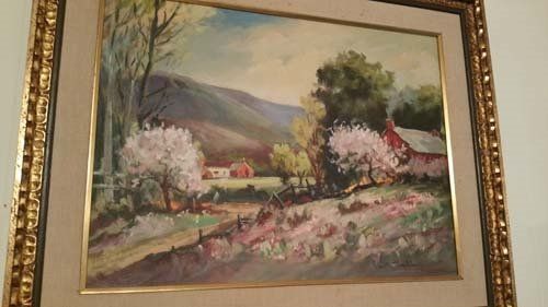 Landscape painting of a valley with blooming trees, a red barn, and mountains in the background. Framed in gold.