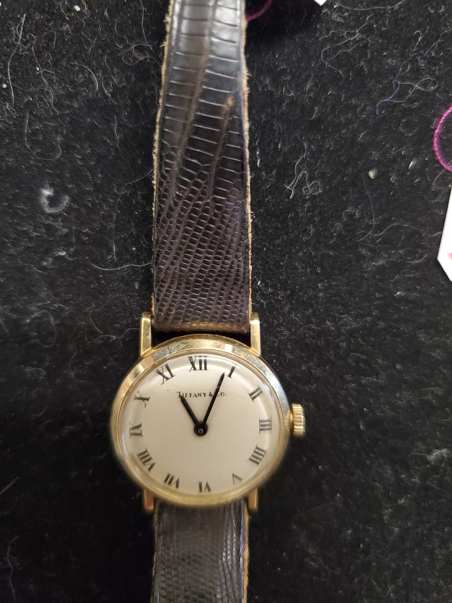 Gold wristwatch with a white face, gold Roman numerals, and a black leather band.