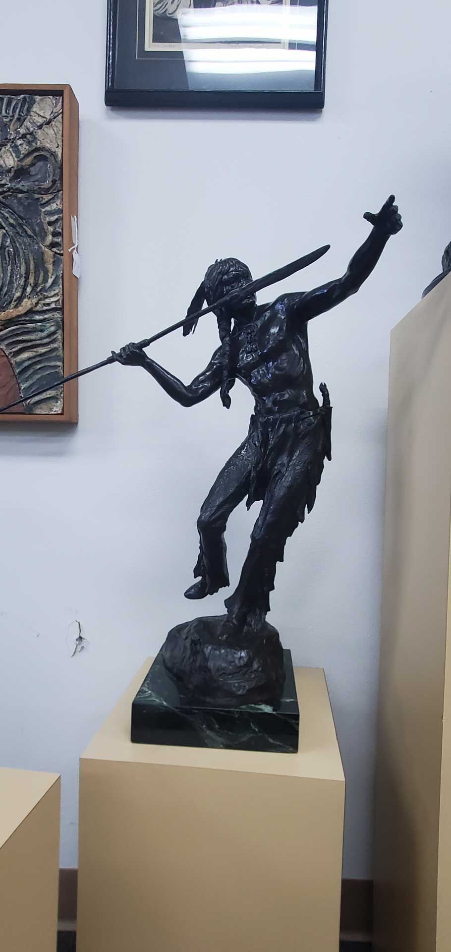 A dark bronze statue of a person with a spear, in a museum setting.
