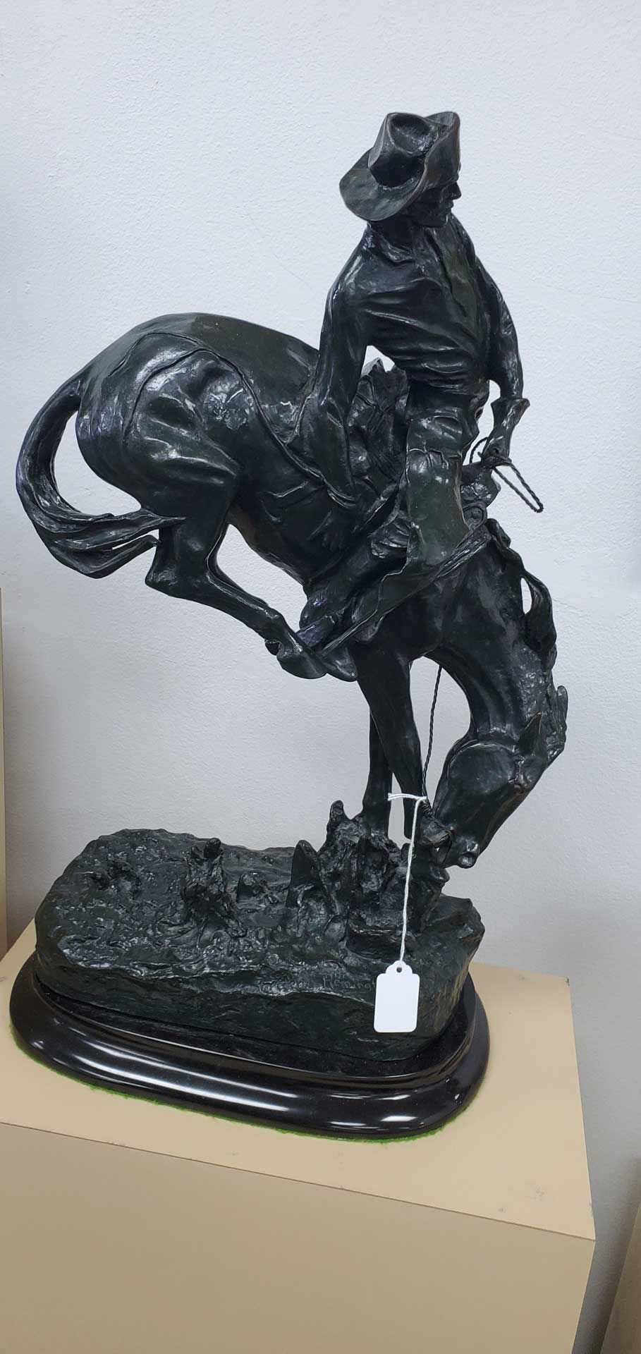 Bronze statue of a cowboy riding a bucking horse, mounted on a wooden base.