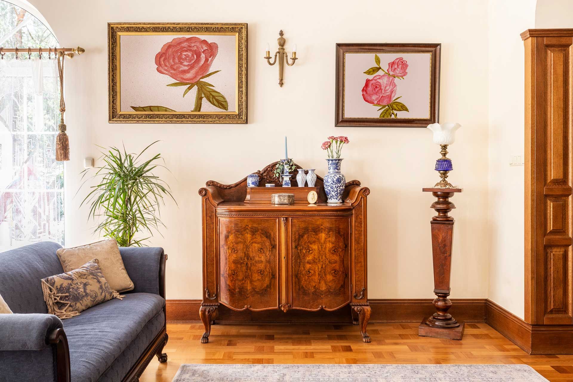Living room with antique furniture, rose paintings, and a blue sofa.