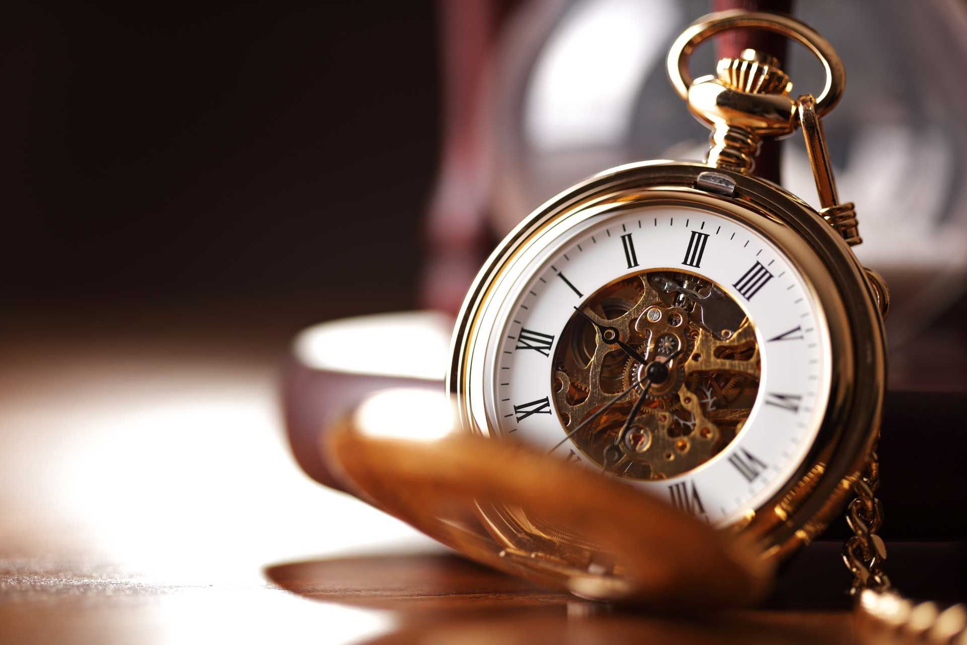 Gold pocket watch open on a wooden surface, with clock face and intricate inner workings visible.