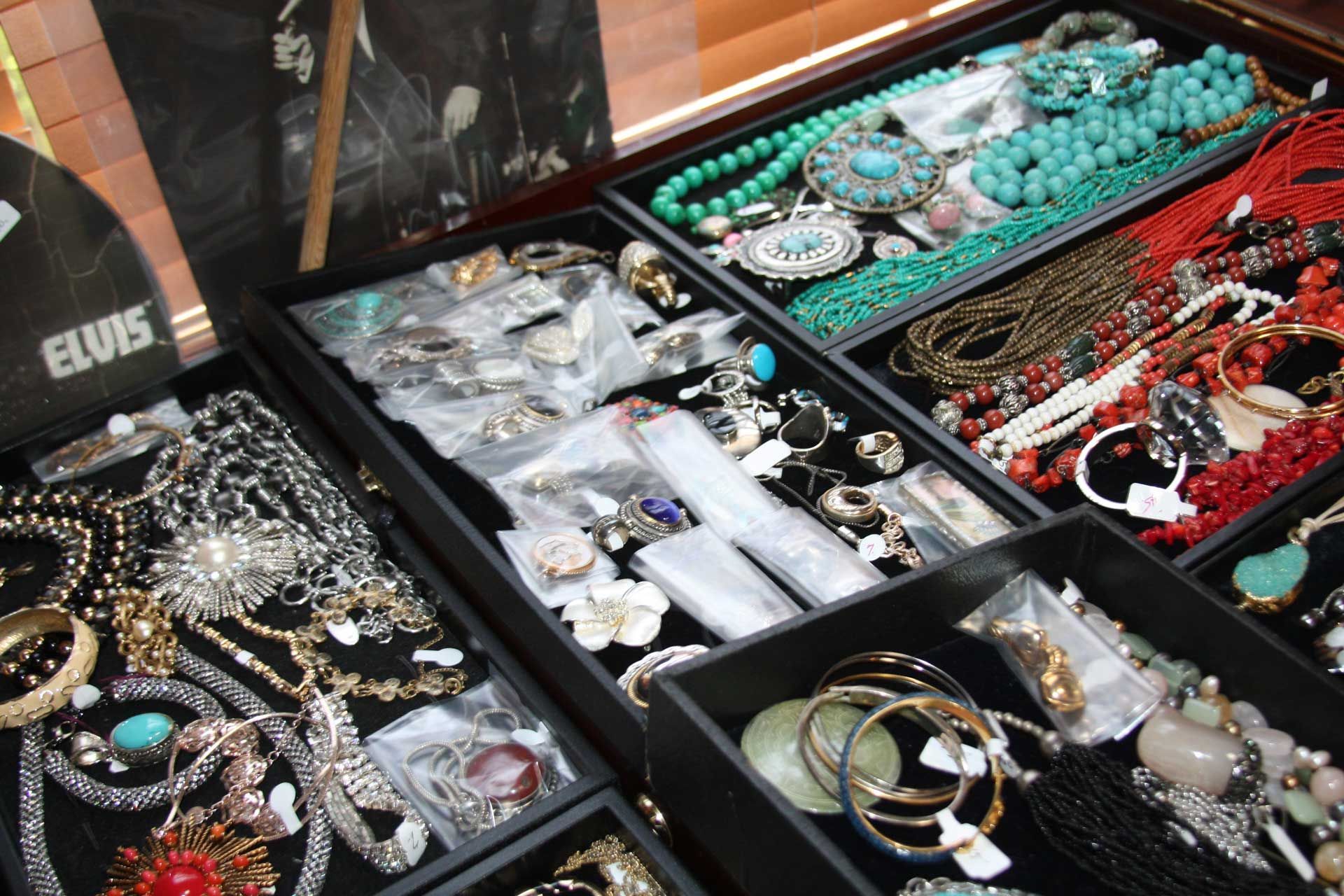 Jewelry display case filled with necklaces, bracelets, and rings in various colors like turquoise, red, and gold.