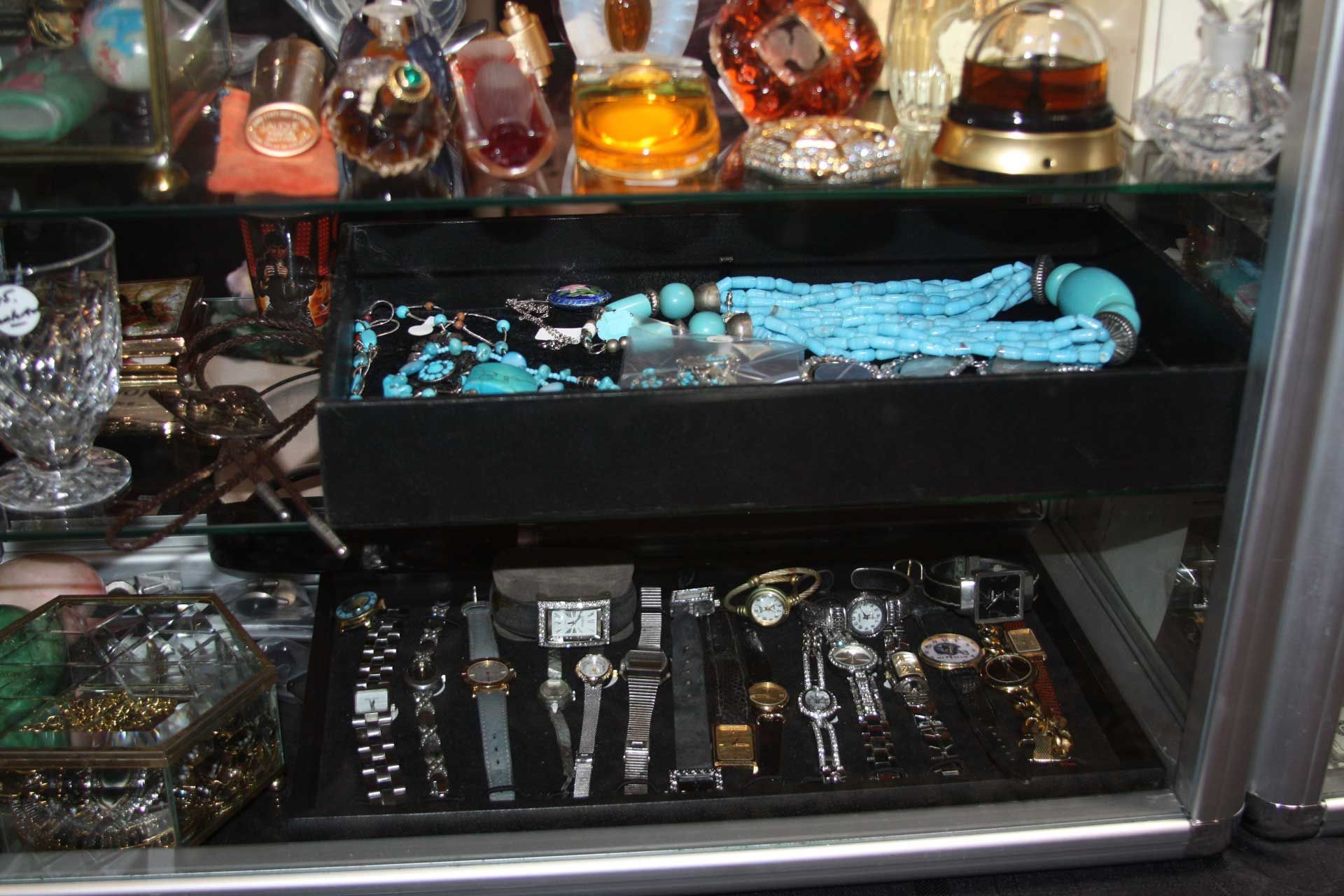 Display case with jewelry and watches: turquoise necklace, various timepieces, and perfume bottles.