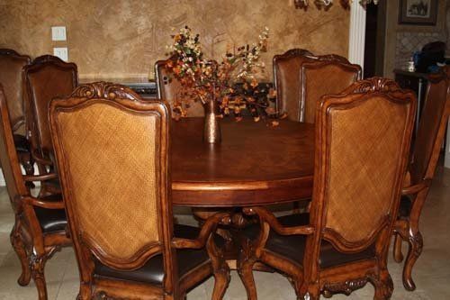 Dining table with eight ornate wooden chairs, arranged around the table, set against a brown wall.