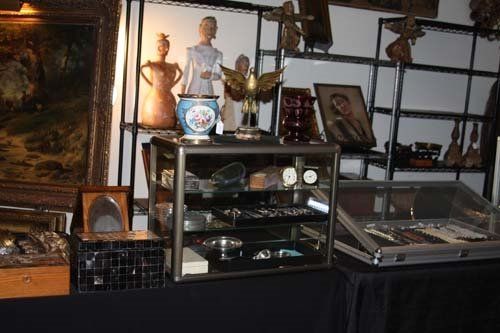 Antique shop display with jewelry, figurines, paintings, and various vintage items.