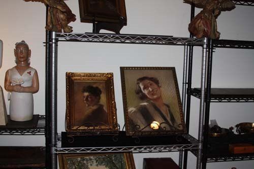 Shelves displaying framed portraits and other art objects in a dim room.