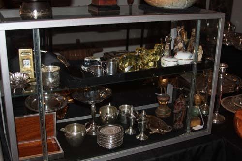 Glass display case filled with silver and gold objects on a black tablecloth.