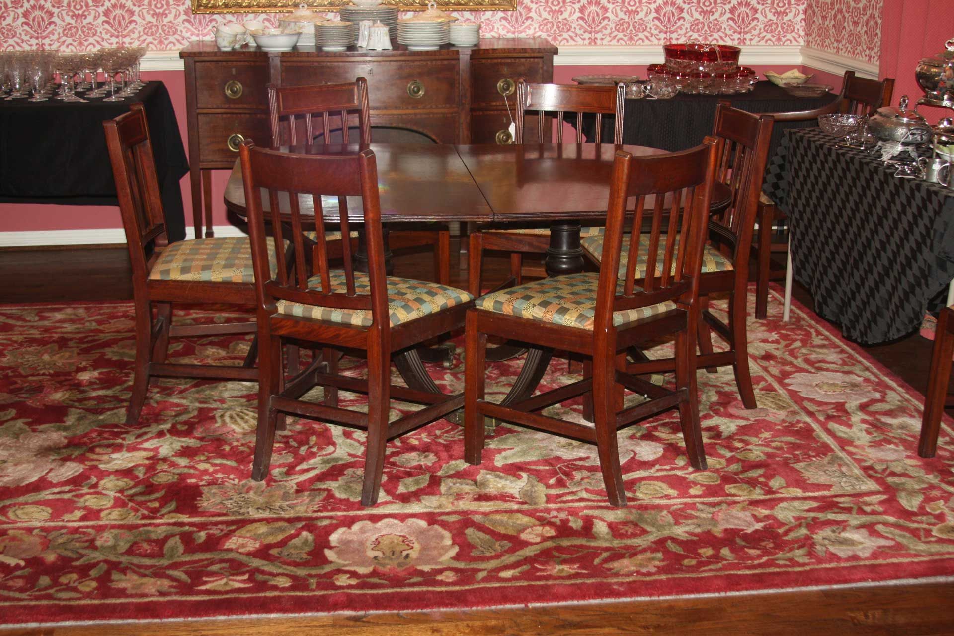 A dining room with a table and chairs on a red patterned rug, with a buffet in the background.