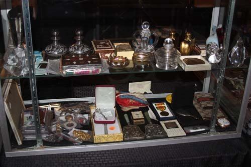 Glass display case filled with antique items: bottles, boxes, silver, and medals.