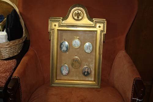 Ornate gold framed shadow box with five miniature portraits on a brown velvet background.