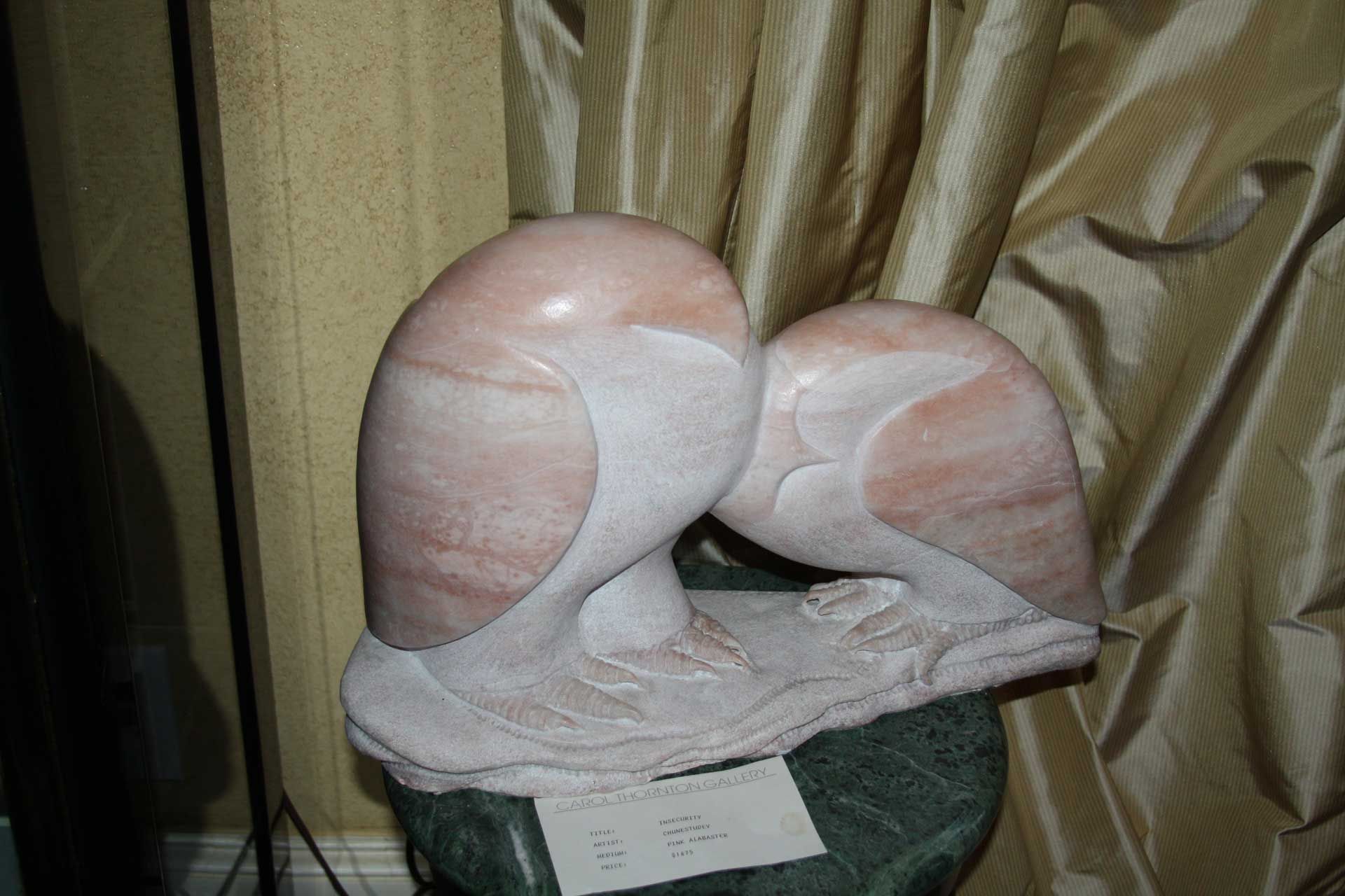 Marble sculpture of two owls, white and pink hues, perched on a branch, set against draped fabric.