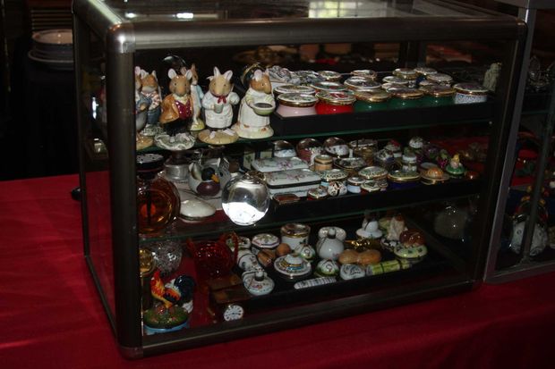 Glass display case with miniature figurines and china on red tablecloth.