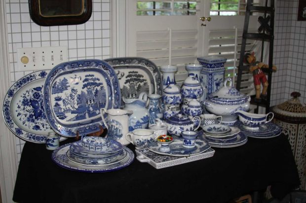 Collection of blue and white china on a black tablecloth, displayed in front of a window and grid-patterned wall.