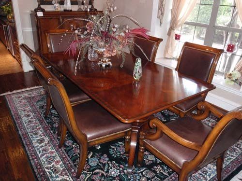 Dining room set: brown wooden table and chairs with leather seats on a floral rug.