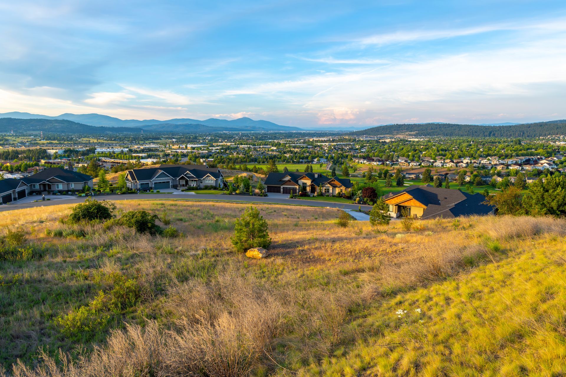 Rolling hillside with houses, town in the distance, blue sky, and mountains.