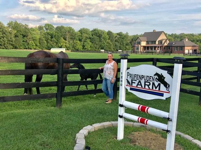 A woman is standing in front of a fence next to a sign for a farm.