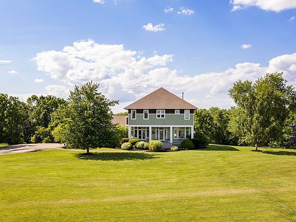 A large house is sitting on top of a lush green field surrounded by trees.