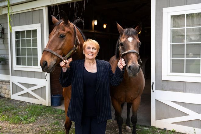 A woman is standing next to two horses in front of a barn.