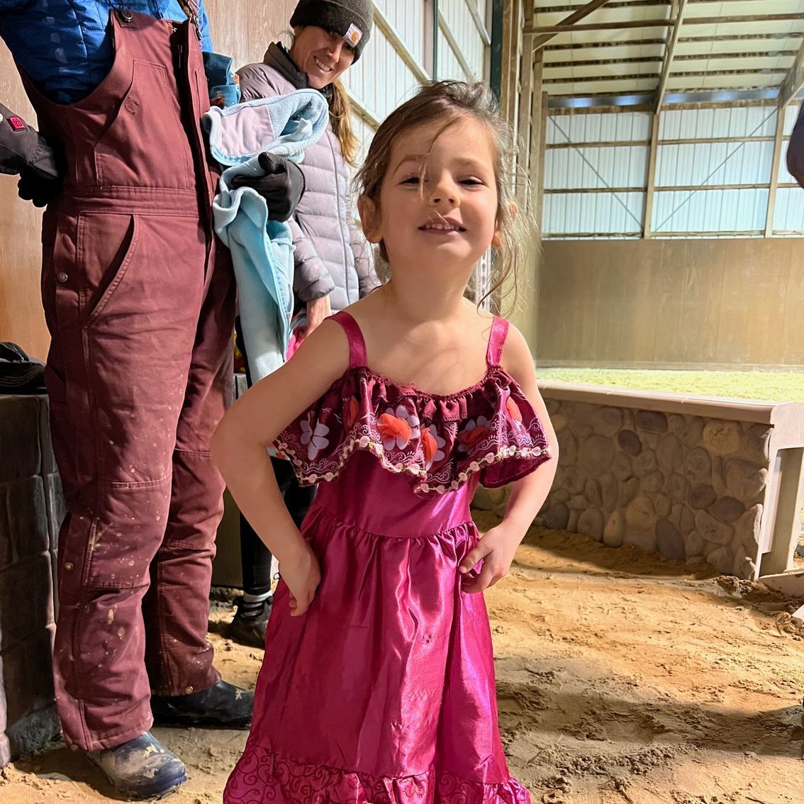 A little girl in a pink dress is standing in the dirt.