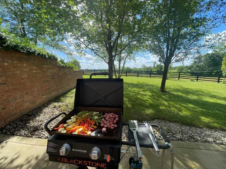 A grill with vegetables on it is sitting on a patio next to a brick wall.