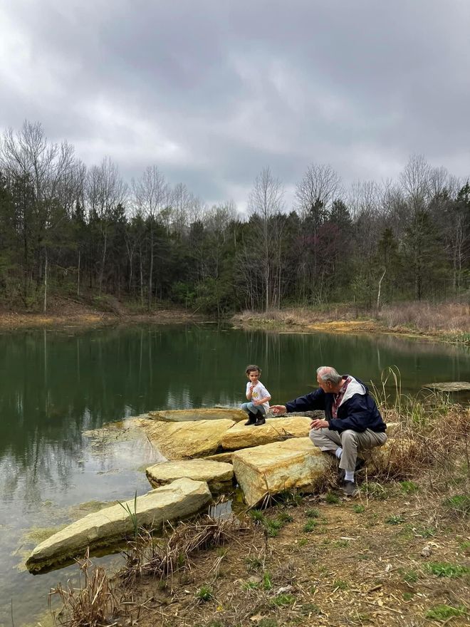 A man and a child are sitting on rocks near a lake.