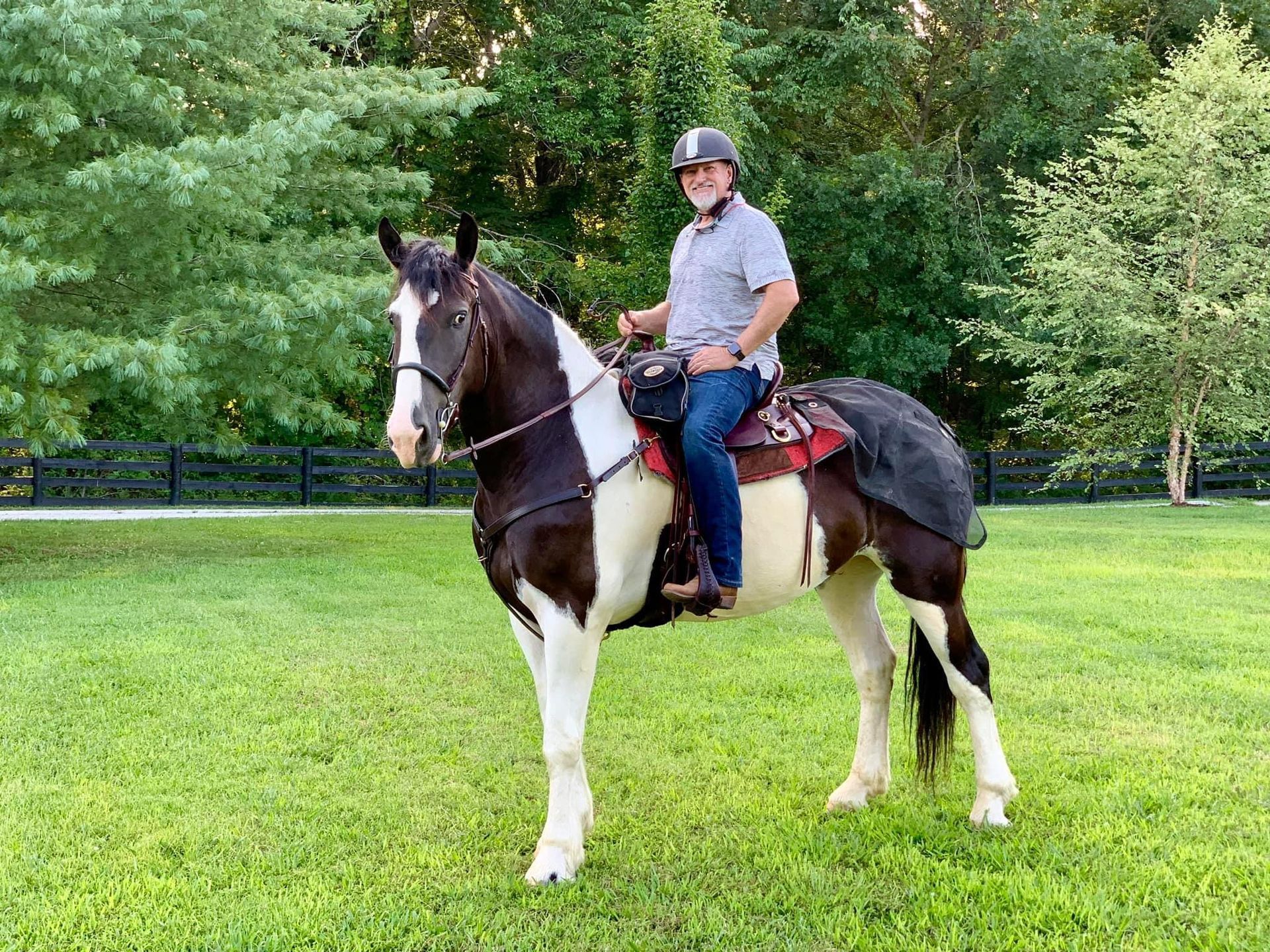 A man is riding a black and white horse in a grassy field.