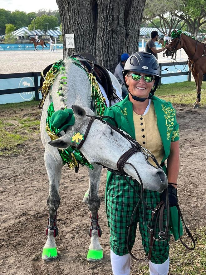 A woman in a green outfit is standing next to a horse.