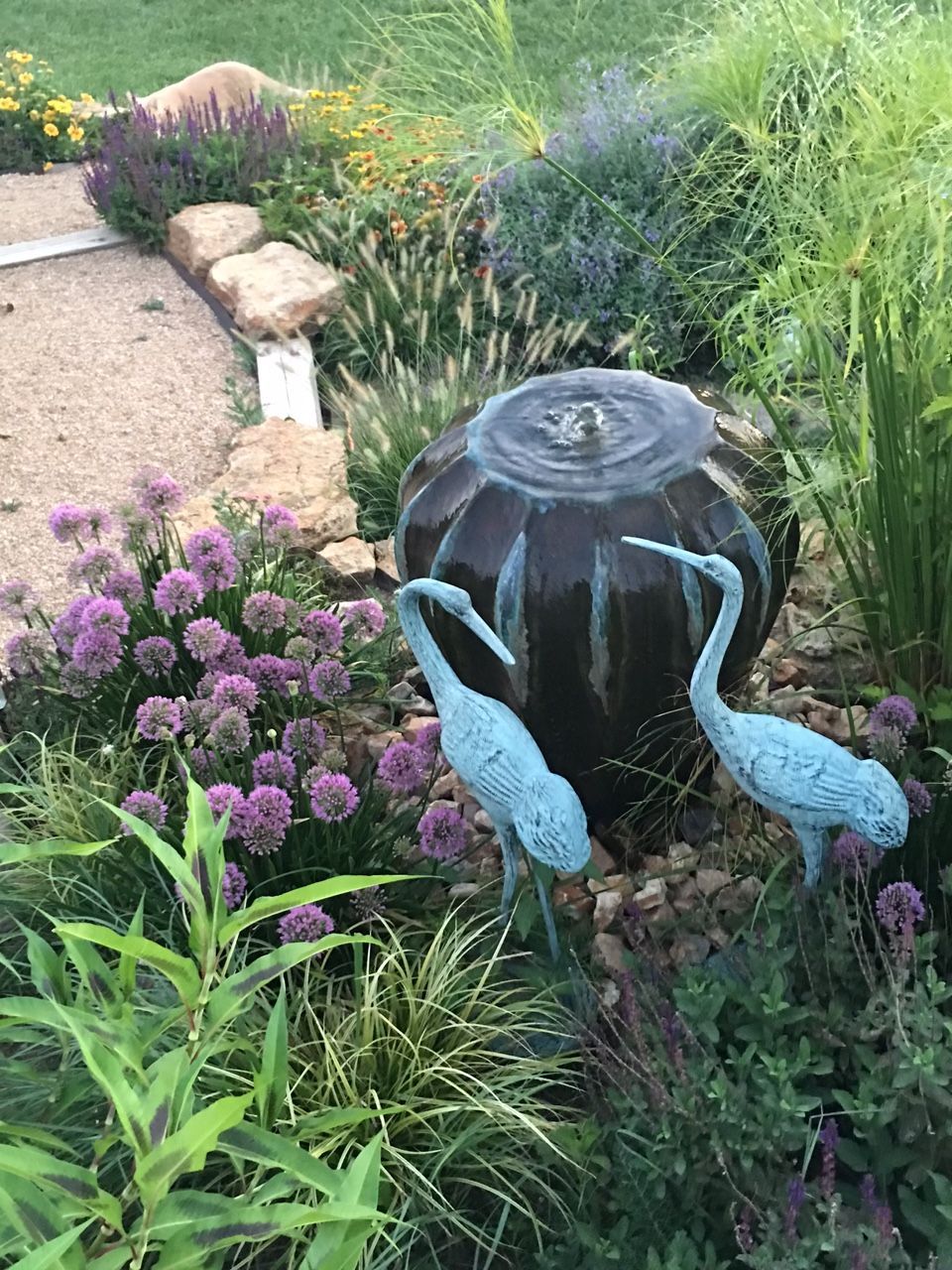 There is a fountain in the middle of the garden with two birds standing next to it.