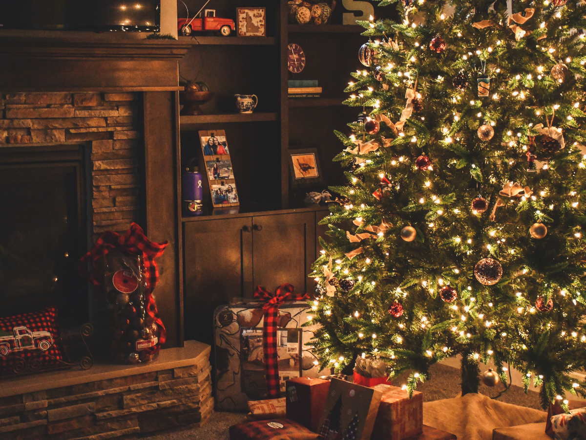 Christmas tree lit with gold lights, presents underneath, fireplace on the left, cozy living room setting.