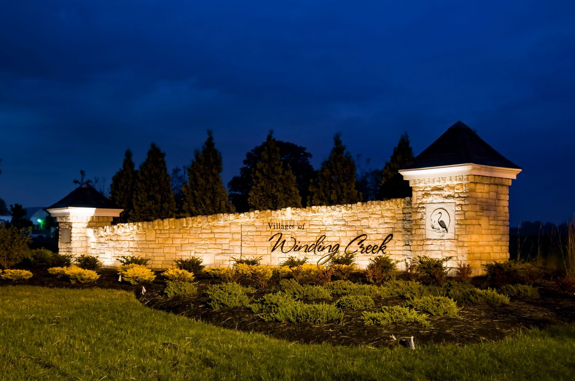 Nighttime view of a stone wall, lit by floodlights with bushes and dark sky.