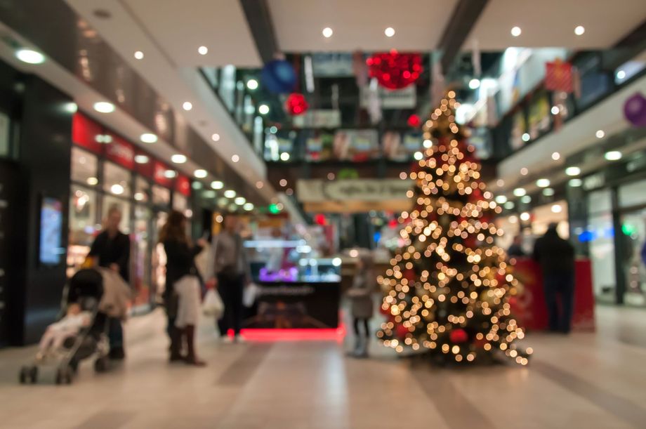 Mall interior with a Christmas tree, people shopping, and festive decorations.