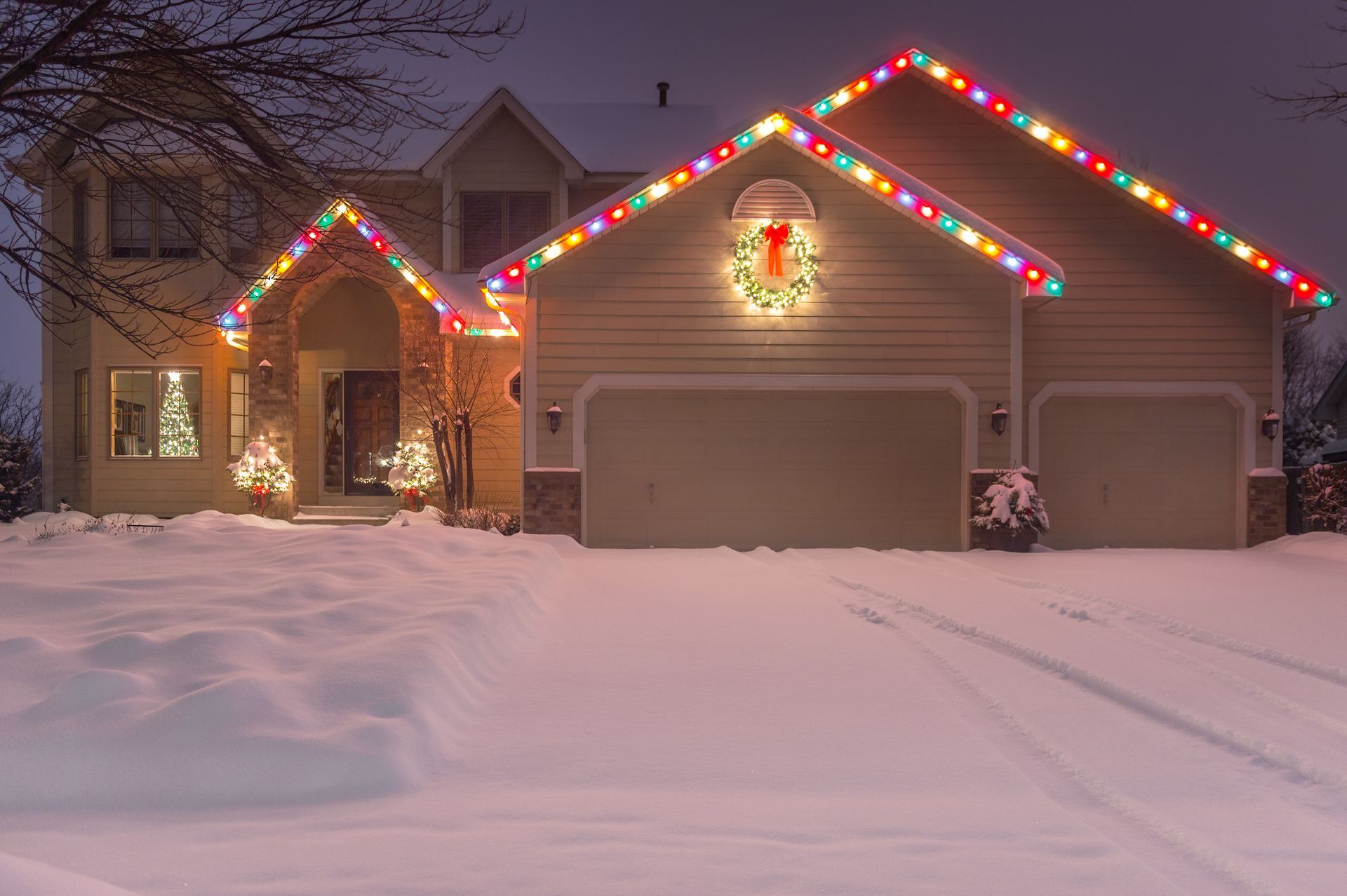 A dark blue house with colorful Christmas lights outlining the roof, and a red car parked nearby.