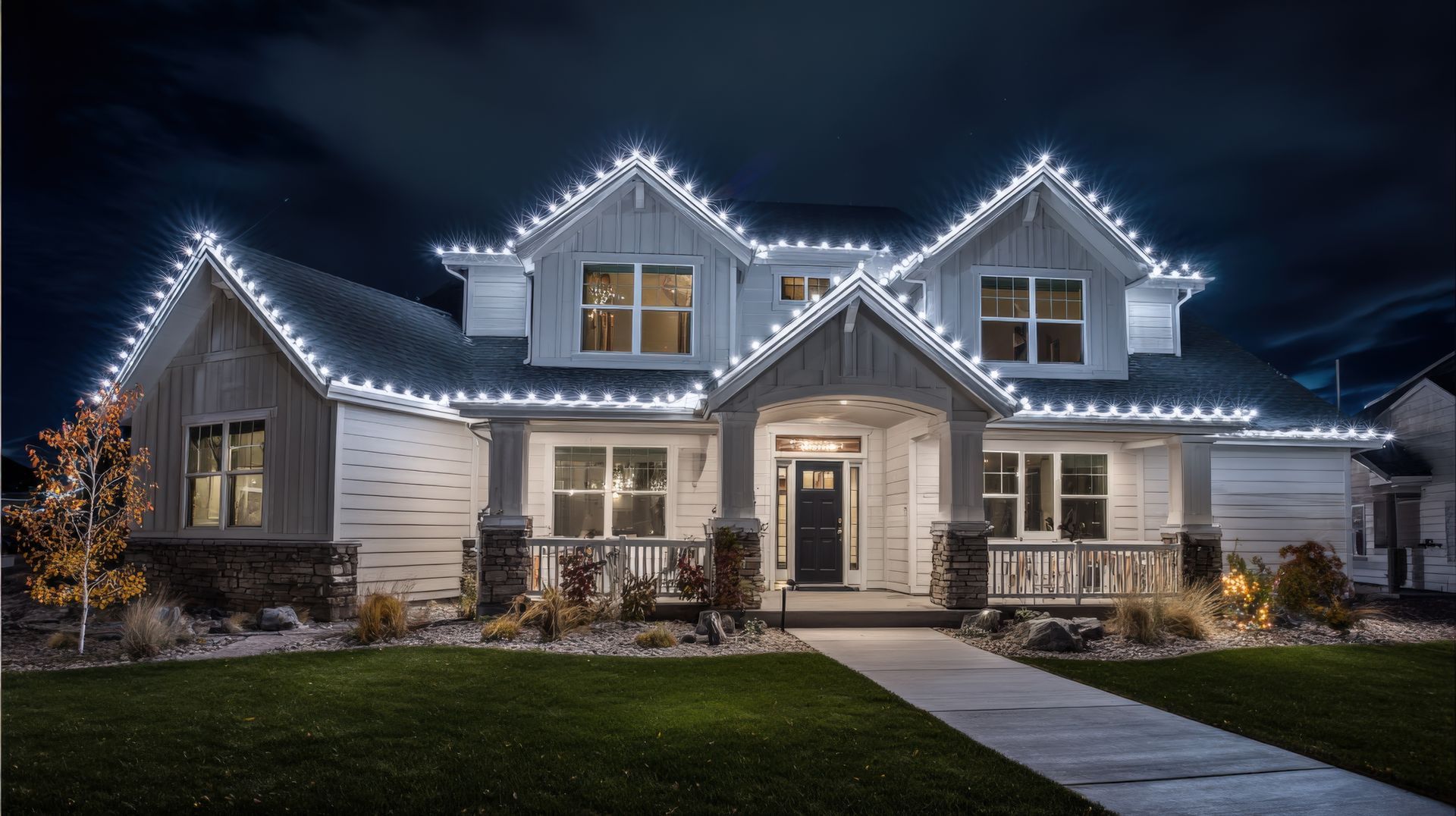 A two-story house at night with white roofline holiday lights, a dark front door, and a grassy front yard.