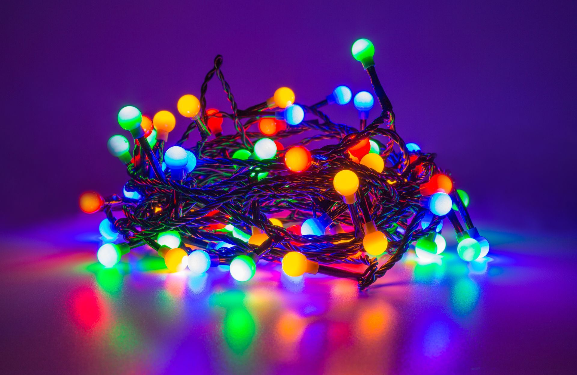 Tangled string of multi-colored LED globe lights on a reflective purple surface.