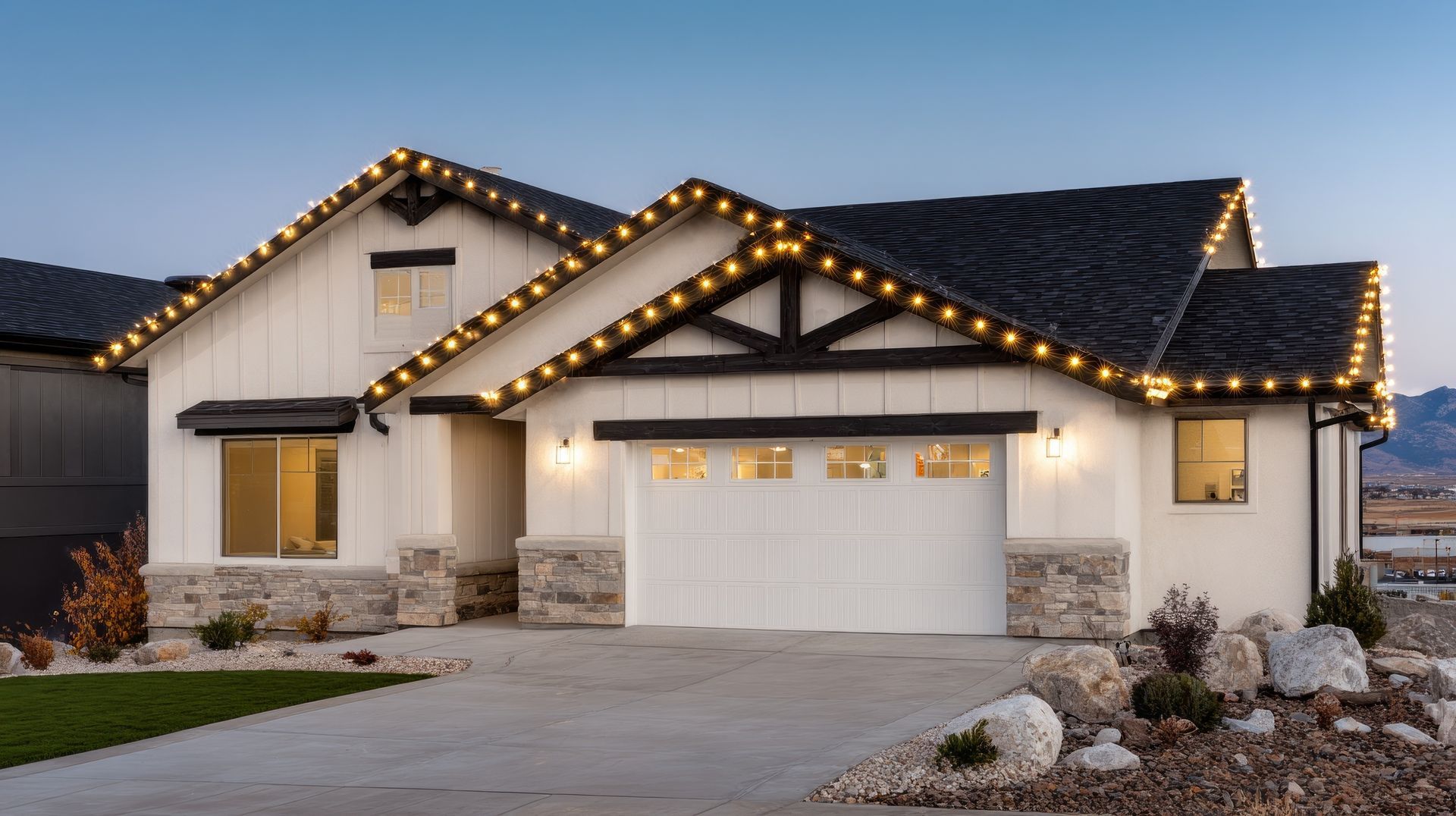 A modern one-story home with white stucco walls, stone trim, and festive LED lights lining the roofline at twilight.