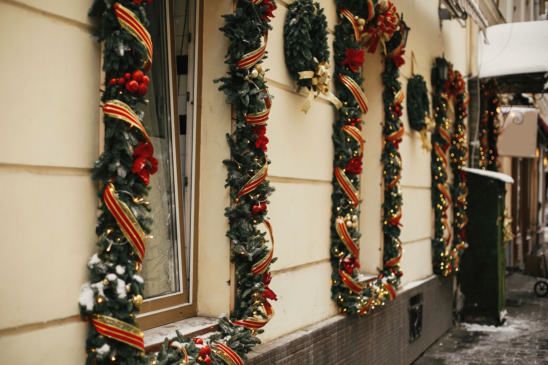 Christmas decorations on a building's exterior: greenery, red bows, gold ribbon, and lights.